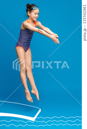 Little girl learning to dive into swimming pool from springboard, blue studio background Little girl learning to dive into swimming pool from springboard, blue studio background 135502861