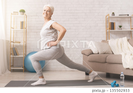Legs stretching. Sporty senior lady doing lunges at home, empty space 135502933