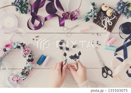 Master making handmade jewelry, top view. Needlewoman workplace with plastic beads, flowers and tools for creating accessories 135503075