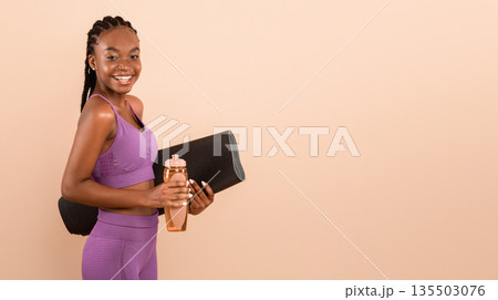 Fitness Workout. Portrait Of Sporty Young African American Woman In Sportswear Holding Yoga Mat And Water Bottle, Cheerful Black Female Ready For Sport Training, Standing Over Beige Background 135503076