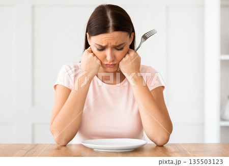 Dieting Concept. Unhappy Woman Looking At Empty Plate Losing Weight Sitting At Table At Home. 135503123