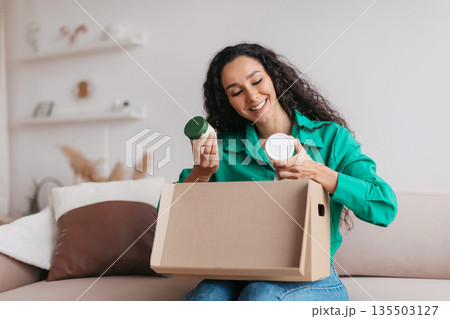 Happy Lady Holding Skincare Cosmetics Products Unpacking Delivered Box After Successful Beauty Shopping Sitting On Couch At Home. Commerce And Delivery Concept 135503127