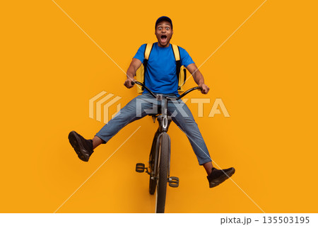Full length of funny black delivery man in blue cap and uniform riding bicycle, wearing yellow thermo backpack bag isolated over bright orange blue studio background. Fast and quick shipment service 135503195