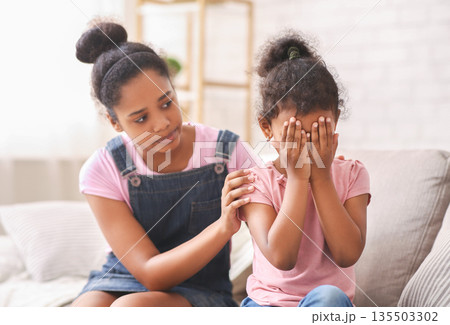 Siblings relationships and support concept. African teen girl embracing crying baby sister, apologizing or comforting her at home 135503302