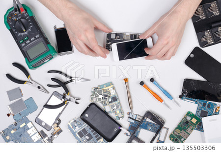 Cell phone repair at service center, smartphone dissasembling and diagnostic, repairman workplace top view Cell phone repair at service center, smartphone dissasembling and diagnostic, repairman workplace top view 135503306