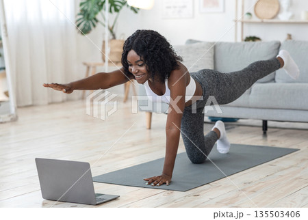 Attractive black woman making morning exercise at home, looking at laptop screen Attractive black woman making morning exercise at home, looking at laptop screen 135503406