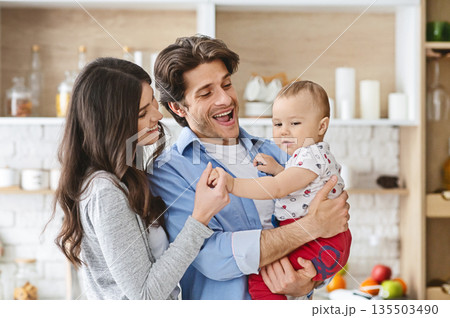 Family happiness. Cheerful parents spending time with adorable baby son in kitchen, free space Family happiness. Cheerful parents spending time with adorable baby son in kitchen, free space 135503490