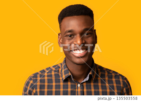 Closeup portrait of positive young African American guy sincerely smiling at camera, cheerful black millennial student guy in checkered shirt standing isolated over yellow background, free space 135503558