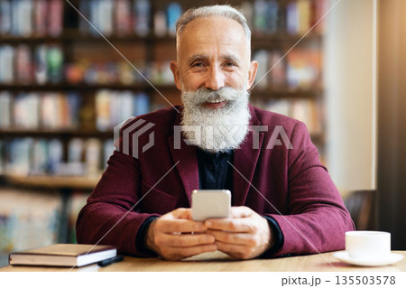 Cheerful elderly grey-haired man with long beard using modern mobile phone while drinking coffee at cafe, chatting with his family or business partners, having notebook by him, free space Cheerful elderly grey-haired man with long beard using modern mobile phone while drinking coffee at cafe, chatting with his family or business partners, having notebook by him, free space 135503578