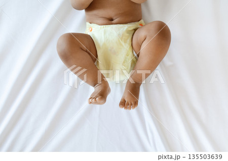 Cropped Shot Of Little African American Baby Wearing Reusable Diaper Lying On Bed, Bottom Part Of Unrecognizable Black Infant Boy Or Girl Resting On White Bedsheet In Bedroom, Top View Cropped Shot Of Little African American Baby Wearing Reusable Diaper Lying On Bed, Bottom Part Of Unrecognizable Black Infant Boy Or Girl Resting On White Bedsheet In Bedroom, Top View 135503639