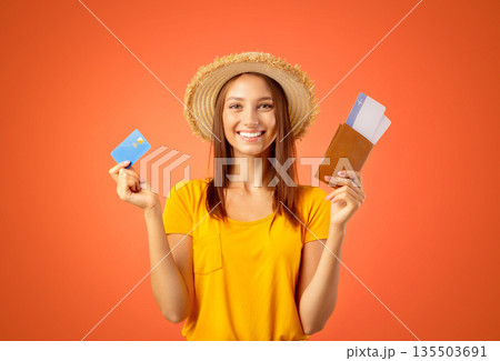 Joyful young woman in summer hat holding passport, flight tickets and credit card, yellow studio background. Happy lady traveller buying plane tickets online, getting loan for vacation or trip Joyful young woman in summer hat holding passport, flight tickets and credit card, yellow studio background. Happy lady traveller buying plane tickets online, getting loan for vacation or trip 135503691