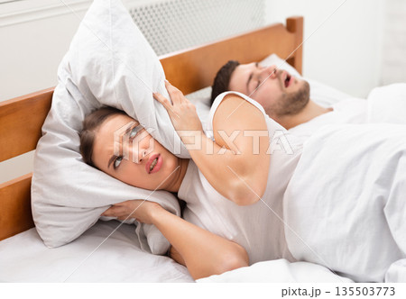 Husband Snoring Bothering Angry Wife Unable To Get To Sleep Covering Ears With Pillow Lying In Bed Indoor. Selective Focus 135503773
