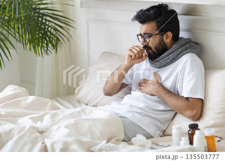 Sick Young Indian Man Coughing While Sitting In Bed At Home, Ill Millennial Eastern Guy Resting In Bedroom, Suffering Bronchitis, Having Seasonal Flu Or Cold Symptoms, Closeup With Free Space 135503777