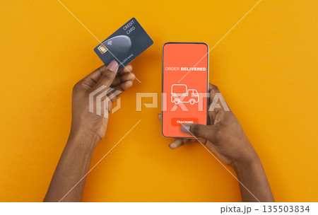 Stay at home, pay with credit card. African american man ordered with online app on cell phone, yellow background Stay at home, pay with credit card. African american man ordered with online app on cell phone, yellow background 135503834