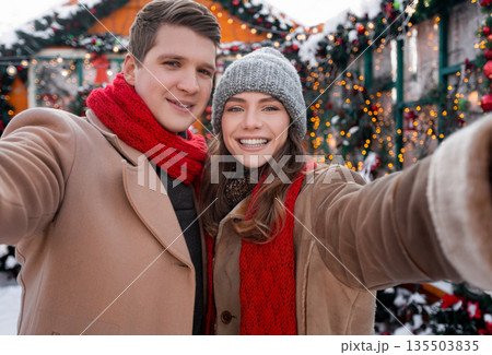 Happy lovers young man and woman taking selfie while spending winter holidays at backyard together, loving millennial couple celebrating Christmas, New Year, decorated street background Happy lovers young man and woman taking selfie while spending winter holidays at backyard together, loving millennial couple celebrating Christmas, New Year, decorated street background 135503835