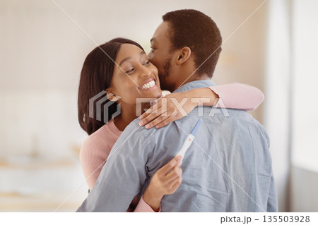 African American man embracing his happy young wife with positive pregnancy test indoors. Millennial black couple expecting baby. Maternity and childbearing concept African American man embracing his happy young wife with positive pregnancy test indoors. Millennial black couple expecting baby. Maternity and childbearing concept 135503928