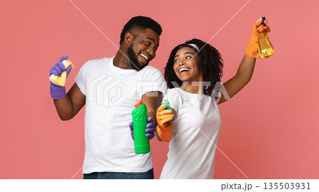 Ready For Spring-Cleaning. Portrait of joyful african couple with household supplies in hands over pink background 135503931