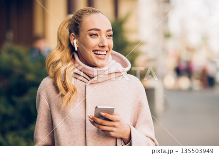 Happy woman walking in city and listening music in airpods, enjoying weekend Happy woman walking in city and listening music in airpods, enjoying weekend 135503949