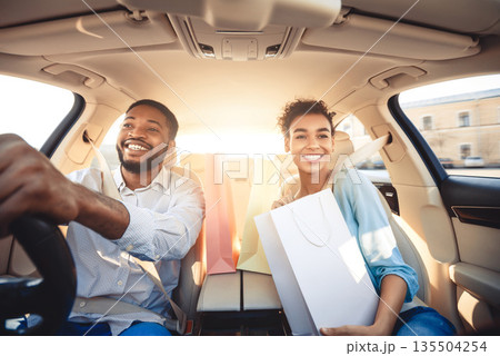Go home after shopping. Couple driving home in car with paper bags, listening music and smiling Go home after shopping. Couple driving home in car with paper bags, listening music and smiling 135504254