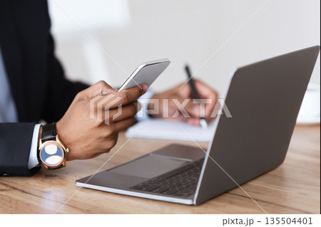 Unrecognizable black manager in suit holding smartphone, taking notes, sitting in front of laptop, office interior, cropped. African american businessman using modern gadgets for business 135504401