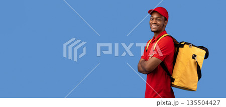 Delivery Service Cocnept. Portrait of confident smiling black male courier wearing red uniform and thermo backpack bag posing with folded arms and looking at camera isolated on blue studio background Delivery Service Cocnept. Portrait of confident smiling black male courier wearing red uniform and thermo backpack bag posing with folded arms and looking at camera isolated on blue studio background 135504427
