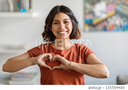 Smiling Young Arab Woman Showing Heart Gesture With Hands Near Chest, Happy Middle Eastern Millennial Lady Making Love Sign At Camera While Standing Indoors In Home Interior, Copy Space 135504483