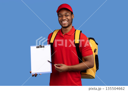 Parcel Receiving. Smiling African American Bearded Delivery Man Holding Pen And Folder With Blank Paper Delivering Goods And Food, Wearing Thermo Bag, Standing Over Blue Studio Background. Mockup Parcel Receiving. Smiling African American Bearded Delivery Man Holding Pen And Folder With Blank Paper Delivering Goods And Food, Wearing Thermo Bag, Standing Over Blue Studio Background. Mockup 135504662