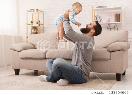 Father and kid spending time together, man throwing up his son at home in living room, copy space Father and kid spending time together, man throwing up his son at home in living room, copy space 135504663