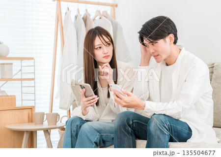 家のリビングに座りスマホを見ながら相談,会話するカップル,夫婦（トラブル,詐欺,悩み,困る） 135504677