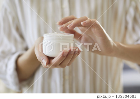 Close up view of female hands holding white jar with body cream Close up view of female hands holding white jar with body cream 135504683