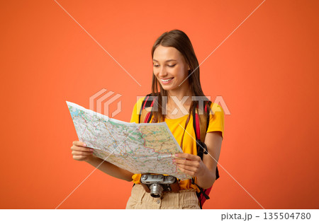 Happy young woman travelling alone, holding city map, having camera and backpack, yellow studio background, copy space. Joyful female traveler looking for new place to go, travelling concept Happy young woman travelling alone, holding city map, having camera and backpack, yellow studio background, copy space. Joyful female traveler looking for new place to go, travelling concept 135504780