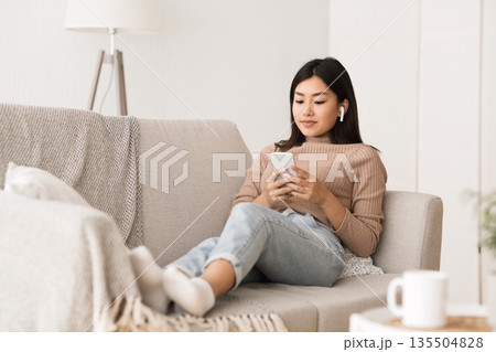 Relaxed girl laying on couch, using phone and listening to music, resting at home Relaxed girl laying on couch, using phone and listening to music, resting at home 135504828