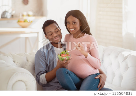 Healthy diet during pregnancy. Happy black boyfriend and his beautiful expectant girlfriend eating tasty vegetable salad at home. Loving pregnant woman having vitamin breakfast Healthy diet during pregnancy. Happy black boyfriend and his beautiful expectant girlfriend eating tasty vegetable salad at home. Loving pregnant woman having vitamin breakfast 135504835