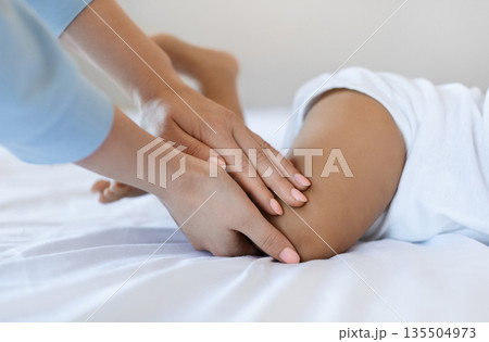 Infant Massage. Unrecognizable Mother Massaging Legs Of Little Black Baby At Home, Caring Mom Gently Stroking Child's Feet While He Lying On Bed At Home, Making Gymnastic With Toddler, Cropped 135504973