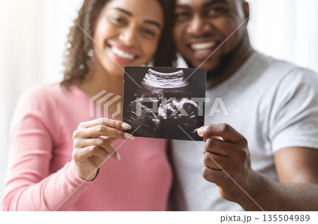 Happy expecting black couple showing ultrasound image of their baby, closeup Happy expecting black couple showing ultrasound image of their baby, closeup 135504989