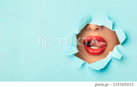Woman with red lips playing with tongue in turquoise paper hole, free space 135505013