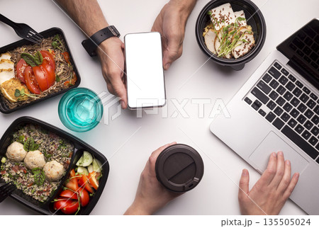 Food on workplace. Delivery of healthy food application in cellphone with white blank space on office table 135505024