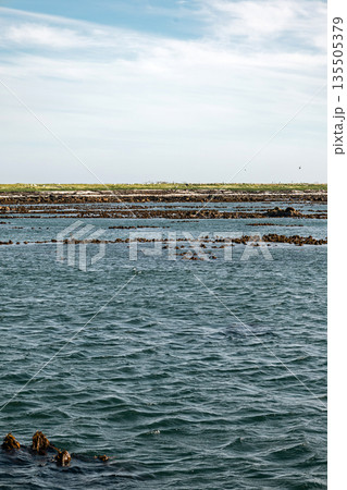 Calm water stretching towards a distant rocky shore under a partly cloudy sky Calm water stretching towards a distant rocky shore under a partly cloudy sky 135505379