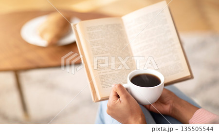 Unrecognizable black lady with coffee reading book, enjoying peaceful morning at home, free space. Cropped view of female hands holding hot beverage and textbook on weekend, indoors Unrecognizable black lady with coffee reading book, enjoying peaceful morning at home, free space. Cropped view of female hands holding hot beverage and textbook on weekend, indoors 135505544
