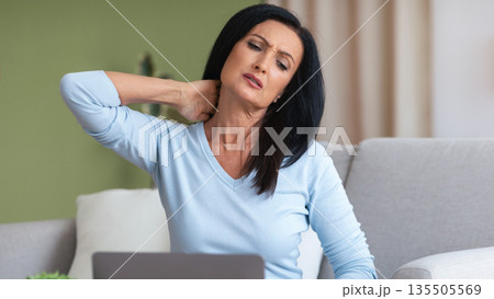 Exhausted Person. Portrait of tired mature lady sitting on the couch massaging sore neck, feeling pain after hard work, copy space. Adult woman suffering from inflammation, taking break at home Exhausted Person. Portrait of tired mature lady sitting on the couch massaging sore neck, feeling pain after hard work, copy space. Adult woman suffering from inflammation, taking break at home 135505569
