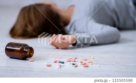 Young woman committing suicide by overdosing on pills, focus on bottle of tablets scattered on floor. Depression and drug overuse, mental breakdown or PTSD problem concept 135505590