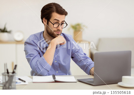 Surpirsed Business Guy In Eyewear Looking At Laptop Having Computer Problem Sitting At Desk In Modern Office. Issue With Internet Connection Concept. Selective Focus Surpirsed Business Guy In Eyewear Looking At Laptop Having Computer Problem Sitting At Desk In Modern Office. Issue With Internet Connection Concept. Selective Focus 135505618