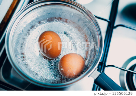 Saucepan stainless steel with two boiling eggs breakfast in a water on a gas stove top view. Saucepan stainless steel with two boiling eggs breakfast in a water on a gas stove top view. 135506129