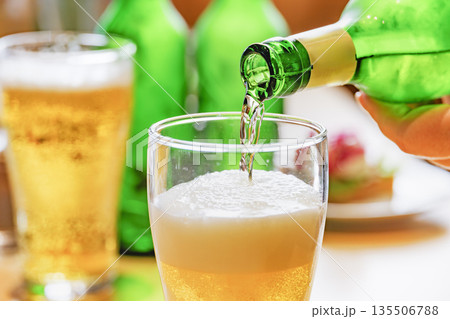 緑のボトルからグラスに注がれる黄金色のビールと泡立つグラス 緑のボトルからグラスに注がれる黄金色のビールと泡立つグラス 135506788