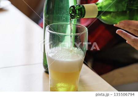 緑のボトルからグラスに注がれる黄金色のビールと泡立つグラス 135506794