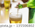 緑のボトルからグラスに注がれる黄金色のビールと泡立つグラス 135506802