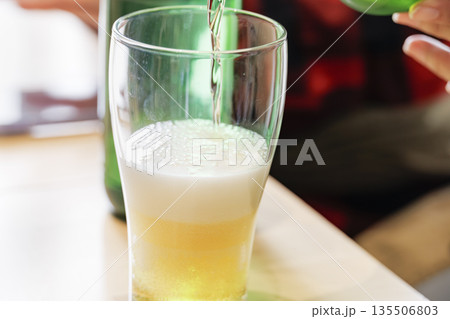 緑のボトルからグラスに注がれる黄金色のビールと泡立つグラス 緑のボトルからグラスに注がれる黄金色のビールと泡立つグラス 135506803