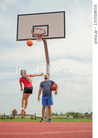 The girl makes a powerful throw into the ring with a ball, making a high jump. A father watches his daughter play basketball. 135508650