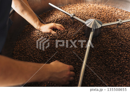 Hand of an unrecognizable male worker checking the temperature of coffee beans in machine drum. Hand of an unrecognizable male worker checking the temperature of coffee beans in machine drum. 135508655