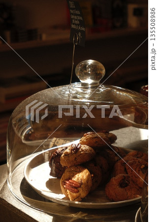 Freshly baked cookies displayed under glass dome in cozy cafe setting with warm lighting Freshly baked cookies displayed under glass dome in cozy cafe setting with warm lighting 135508986